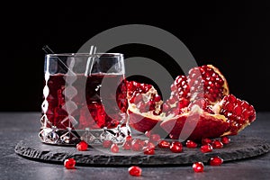 A composition of a pomegranate drink and cut garnet on a black background. Healthful and fresh red cocktails.