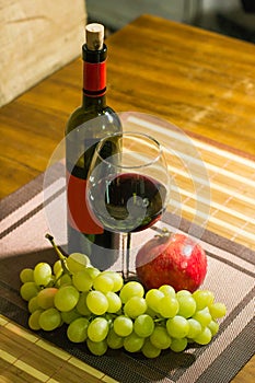 Composition of pomegranate, yellow muscat grape, glass and bottle of red wine on a wooden board