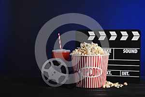 Composition with popcorn, cinema clapperboard and film reel on table against color background