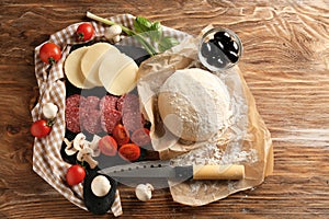 Composition with raw dough and ingredients for pizza on wooden background