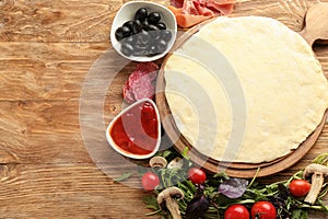 Composition with raw dough and ingredients for pizza on wooden background