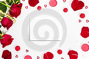 Composition of red roses, rose petals, sequin hearts, candles, gold ribbons, blank card on white background. Content for Birthday