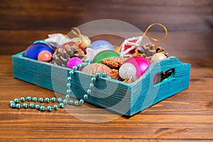 composition of retro wooden box with Christmas decoration, tinsel, pinecones, stars, balls and beads on wooden background, close