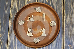 Composition of romantic meetings from vintage wooden figures and decorative flowers from satin on ceramic dish. Dark rough wooden