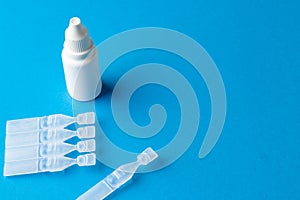 Composition of saline solution caplets and dropper bottle on blue background with copy space