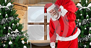 Composition of santa claus carrying gift sack by christmas trees against window, copy space