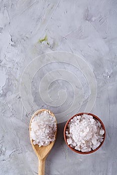 Composition of sea salt in ceramic bowl and spoon for cooking or spa on white background, top view, selective focus