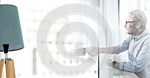 Composition of senior businessman and colleague shaking hands in meeting room with double exposure