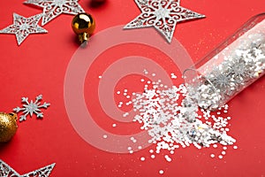 Composition with shiny confetti spilled out of champagne glass near Christmas decorations on red background, closeup