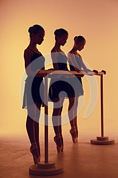 Composition from silhouettes of three young dancers in ballet poses on a orange background.