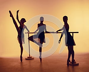 Composition from silhouettes of three young dancers in ballet poses on a orange background.