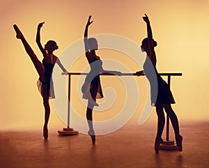 Composition from silhouettes of three young dancers in ballet poses on a orange background.