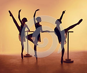 Composition from silhouettes of three young dancers in ballet poses on a orange background.