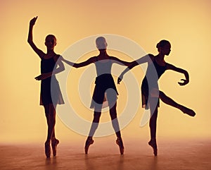 Composition from silhouettes of three young dancers in ballet poses on a orange background.