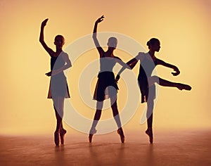 Composition from silhouettes of three young dancers in ballet poses on a orange background.