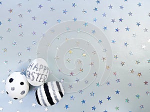 Composition of silver glitter inscription Happy Easter on white egg and metallic stars spangles sequins. Eggs with black and