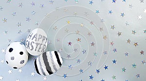 Composition of silver glitter inscription Happy Easter on white egg and metallic stars spangles sequins. Eggs with black and