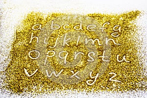 A composition with small letters of the alphabet on beautiful gold glitter. Background and texture of gold glitter. Luxury gold