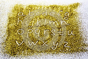 A composition with small letters of the alphabet on beautiful gold glitter. Background and texture of gold glitter. Luxury gold