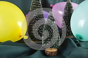 a composition of snowy Christmas trees surrounded by multicolored balloons on a wavy green background