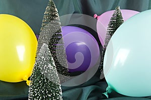 a composition of snowy Christmas trees surrounded by multicolored balloons on a wavy green background