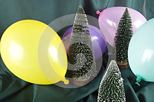 a composition of snowy Christmas trees surrounded by multicolored balloons on a wavy green background