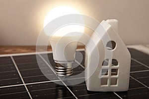 Composition with solar panel, led lamp, money and house model on brown table.