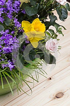 Composition of spring flowers and grass in a green glass bowl on a light wooden background with visible grain