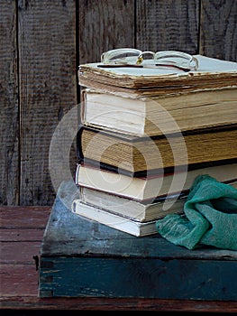 The composition of a stack of old books and glasses on a wooden background. Vintage photo.