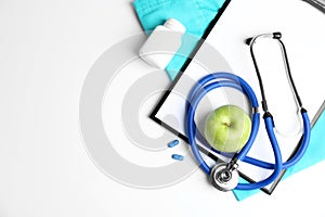 Composition with stethoscope, apple and clipboard on light background. Medical equipment