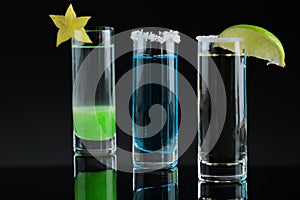 A composition of three colorful shot drinks. Alcoholic cocktails with decorative fruits on a black background. Copy