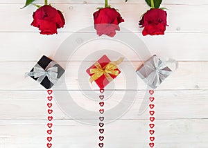 Composition of three red roses, handmade gift box, bows, sequins hearts on wooden table. Content for Birthday, Valentines Day,