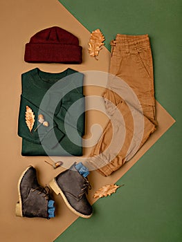 Composition of toddler boy warm clothes, shoes and a toy on color background.