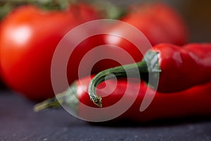 Composition of tomato bunch and hot pepper on black piece of board, top view, close-up, selective focus.