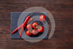 Composition of tomato bunch and hot pepper on black piece of board, top view, close-up.