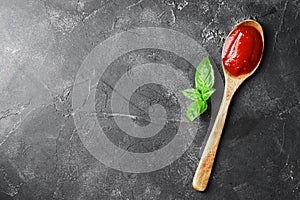 Composition of tomato sauce in a wooden spoon and basil on a dark