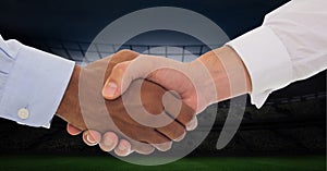 Composition of two businessmen shaking hands over sports stadium