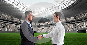 Composition of two businessmen shaking hands over sports stadium