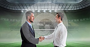 Composition of two businessmen shaking hands over sports stadium