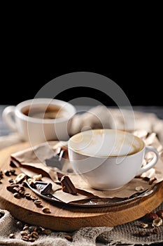 Composition with two glass of cappuccino and served with coffee beans and chocolate on wooden chopping board