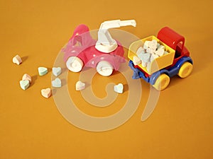 A composition of two toy cars, in the back are vitamin tablets in the shape of hearts, sweet tablets are scattered on a bright ba