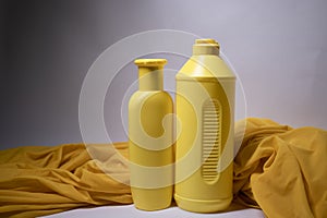 Composition of two yellow shampoo bottles with no label in a silk yellow fabric.body care and beauty concept. Copy space