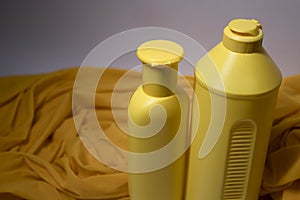 Composition of two yellow shampoo bottles with no label in a silk yellow fabric.body care and beauty concept. Copy space