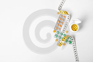 Composition with Weight loss pills and measuring tape on white background, top view.