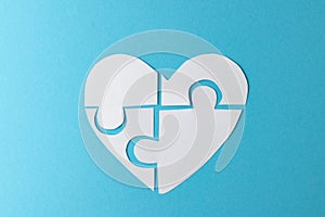 Composition of white heart made of jigsaw puzzle pieces on blue background, with copy space