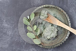 Essential oil with cosmetic clay and cornflower and branch of eucalyptus, stones, for spa treatments, in wood spoon, on photo