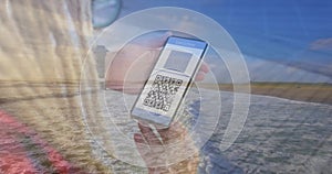 Composition of woman holding a smartphone with qr code on screen against aerial view of the beach