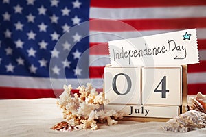 Composition with wooden calendar and card on sand against USA flag. Happy Independence Day