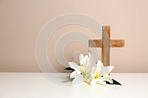 Composition with wooden cross and blossom lilies on table against color background