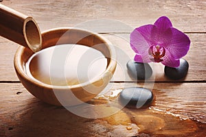 Composition on a wooden table with a bamboo stem and a bowl of water, stones for spa procedures and a bright orchid flower.